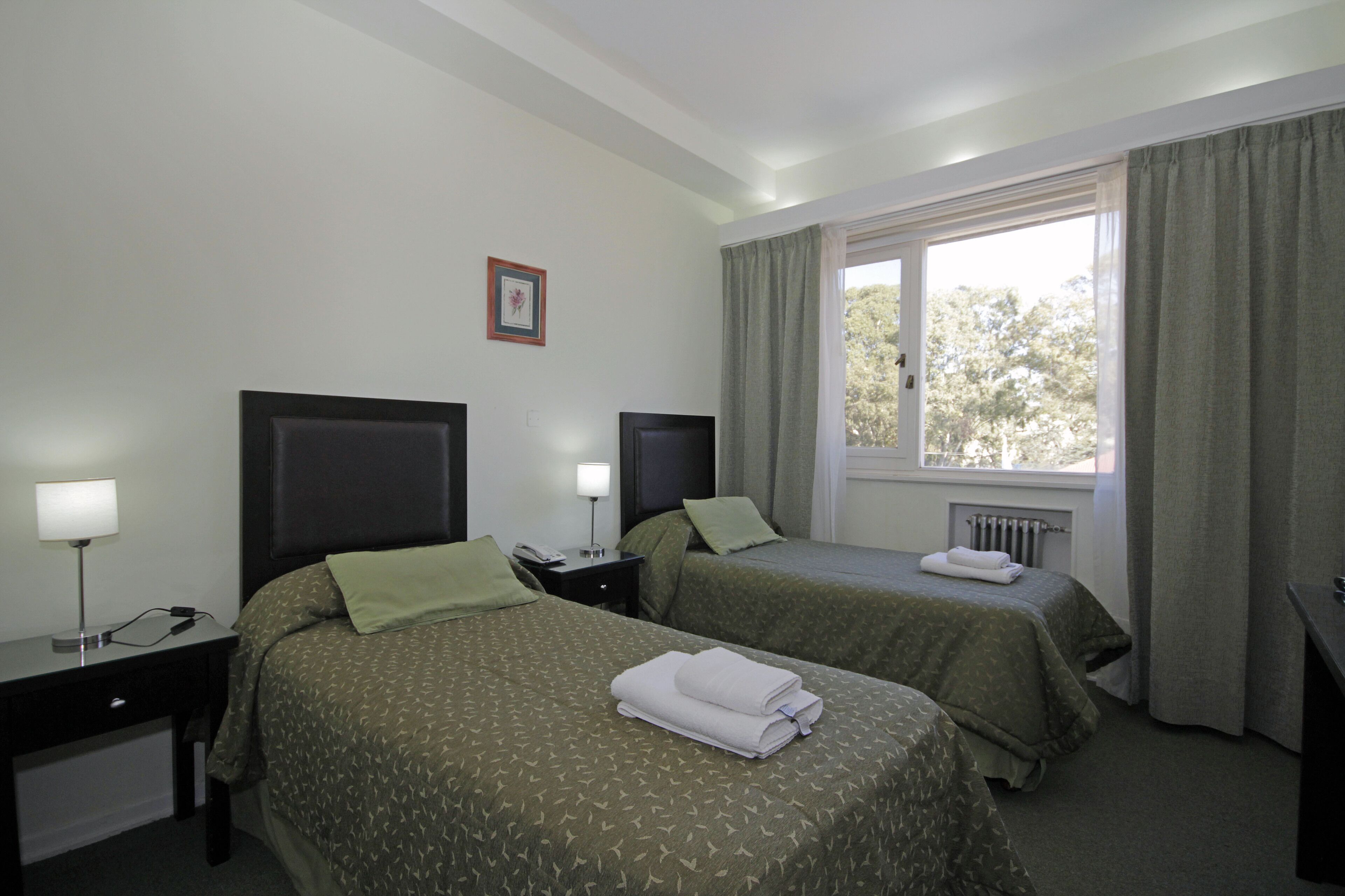 A hotel room with two beds, a desk, a lamp, and a window with curtains.