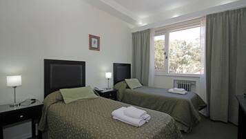 Habitación de hotel con dos camas, un escritorio, una lámpara y un ventanal con cortinas.