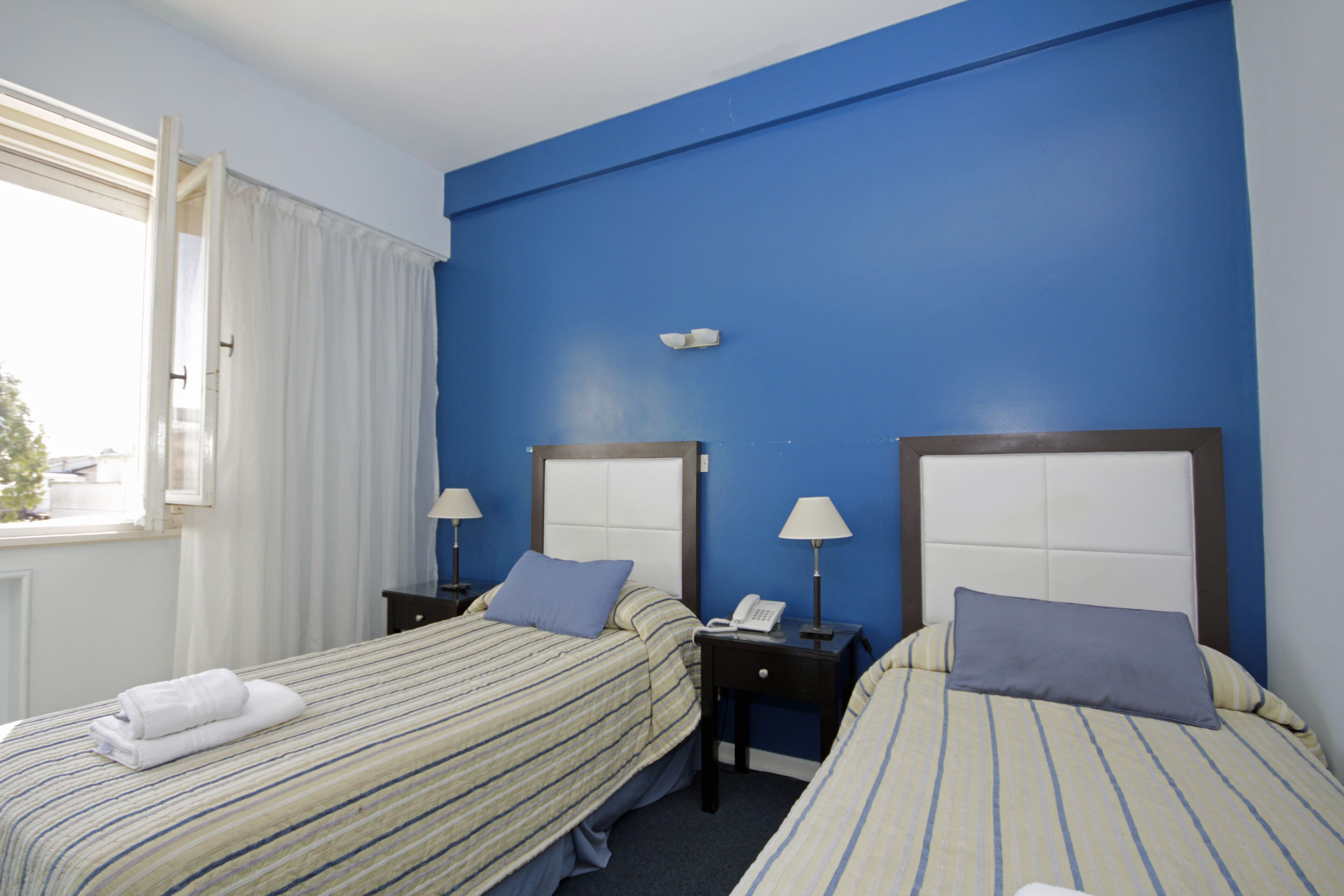 Ein Hotelzimmer mit zwei Betten, jeweils mit Kopfteil, Nachttischen mit Lampen und einem fenster mit Vorhängen.