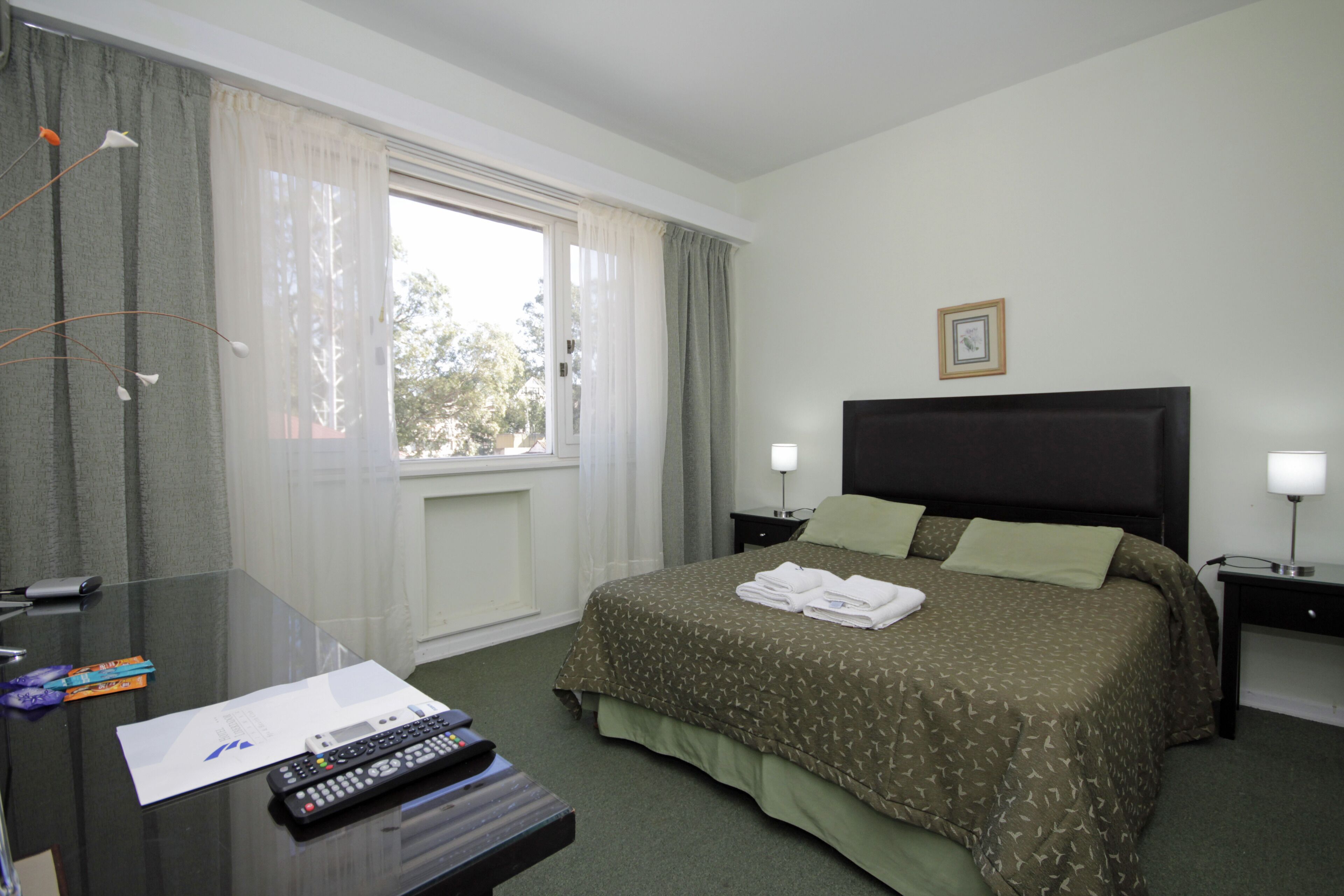 Een hotelkamer met een bed, nachtkastjes, een bureau met een afstandsbediening en een raam met gordijnen.