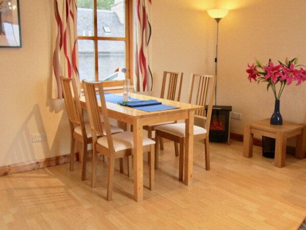 A dining area with a wooden table and chairs, a vase with flowers, and a lamp.