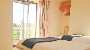 A hotel room with two beds, a view of a car and a garden through a sliding door. - Dolphin Bay Suites (Inverness)