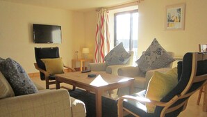 A living room with a flat-screen TV mounted on the wall, a coffee table, two sofas with patterned cushions, and a window with curtains. - Dolphin Bay Suites (Inverness)