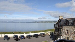 A coastal building with a stone facade, multiple balconies, and a parking area with several cars. - Dolphin Bay Suites (Inverness)