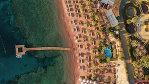 An aerial view of a beach resort with a swimming pool, sun loungers, and a pier extending into the water.