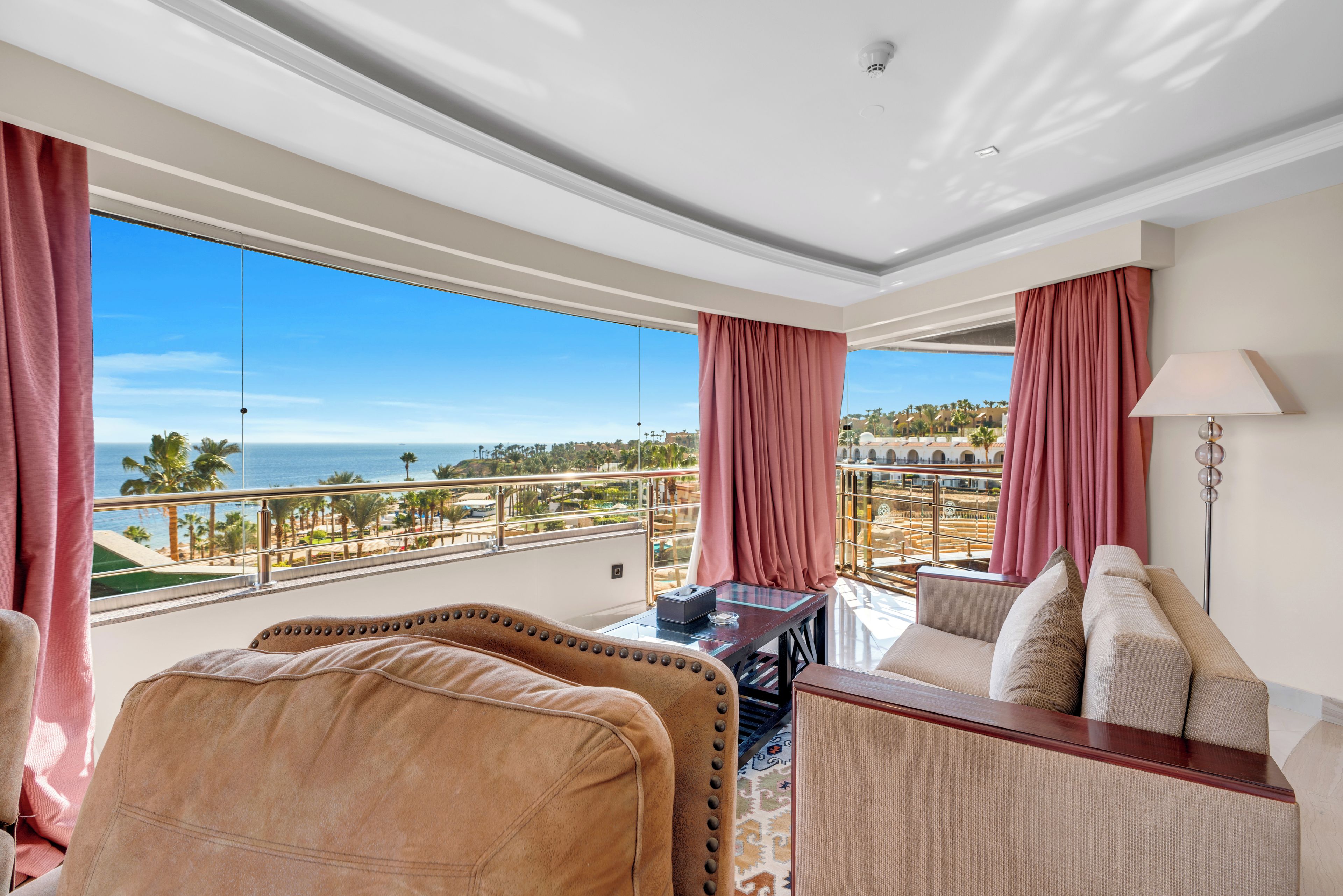 A hotel room with a balcony overlooking a beach and resort area.