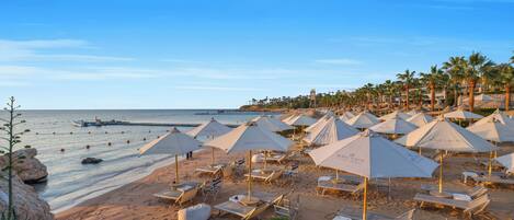 A beach with rows of sun loungers and umbrellas, a wooden deck, and a view of the sea.