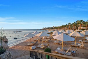 Una playa con filas de tumbonas y sombrillas, una terraza de madera y vista al mar.