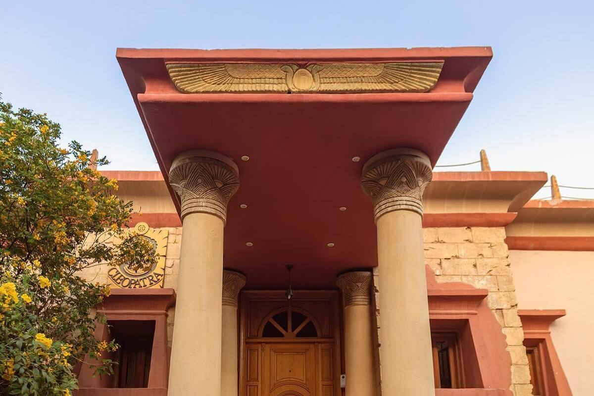 A building with a prominent entrance featuring a large wooden door, flanked by two columns with intricate capitals, and a red roof with decorative elements.