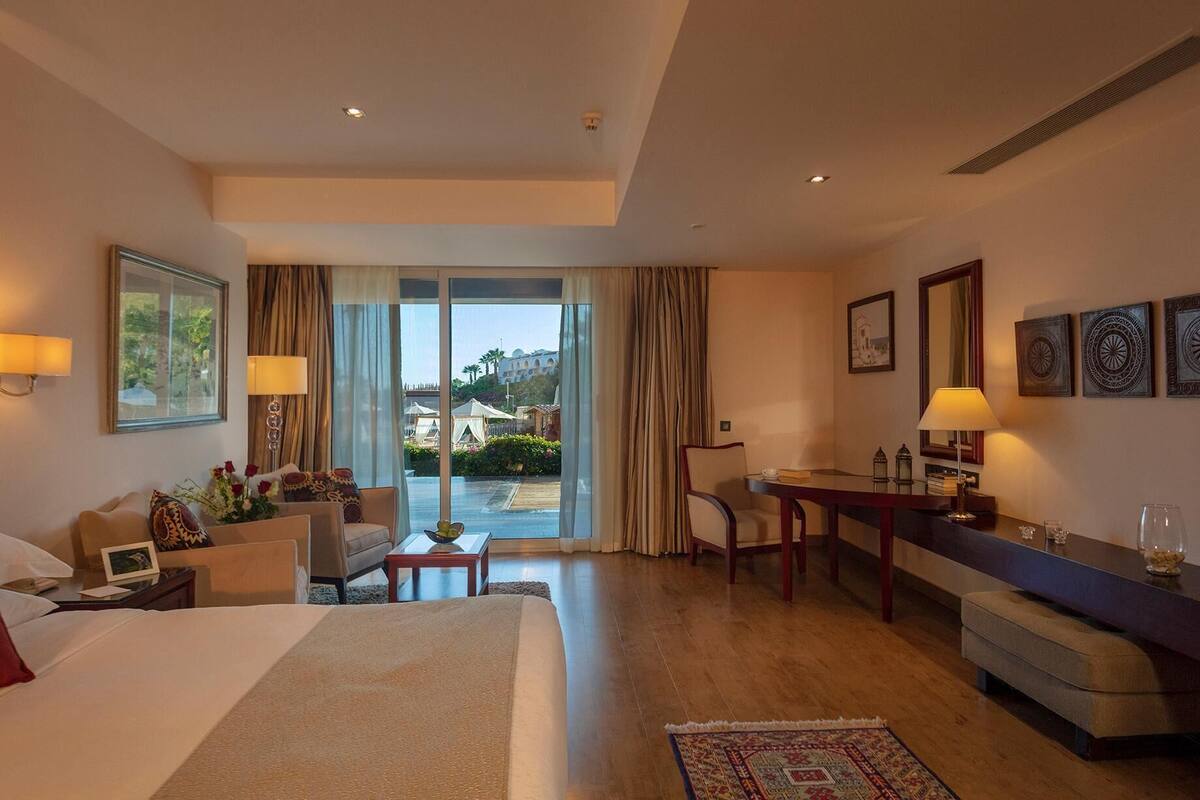 A hotel room with a bed, a desk, a chair, a sofa, and a view of the outdoors.