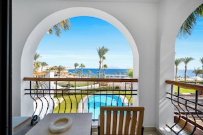 Un balcó amb vista a una piscina, palmeres i l'oceà.
