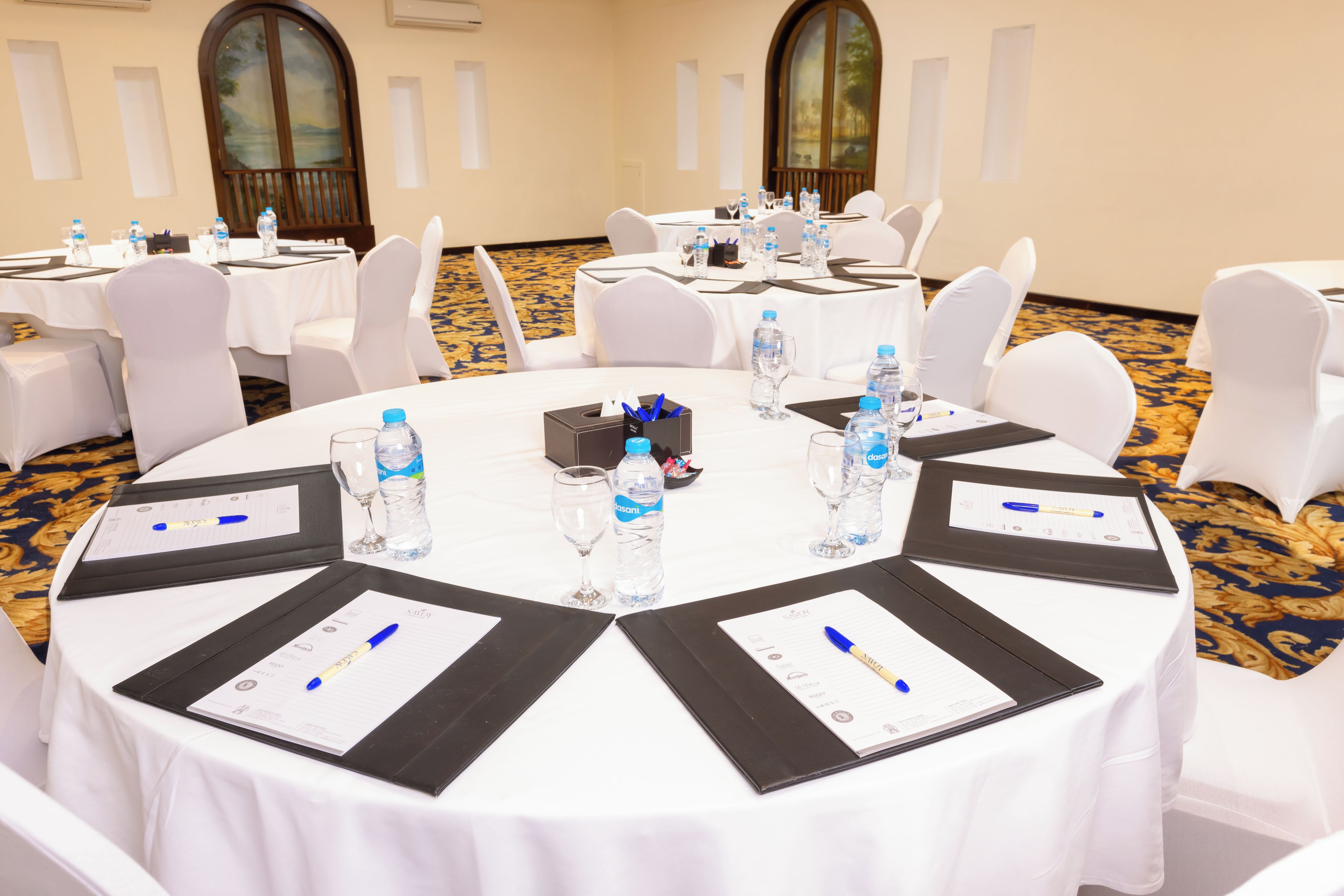 A conference room with round tables, white chairs, water bottles, and nameplates.