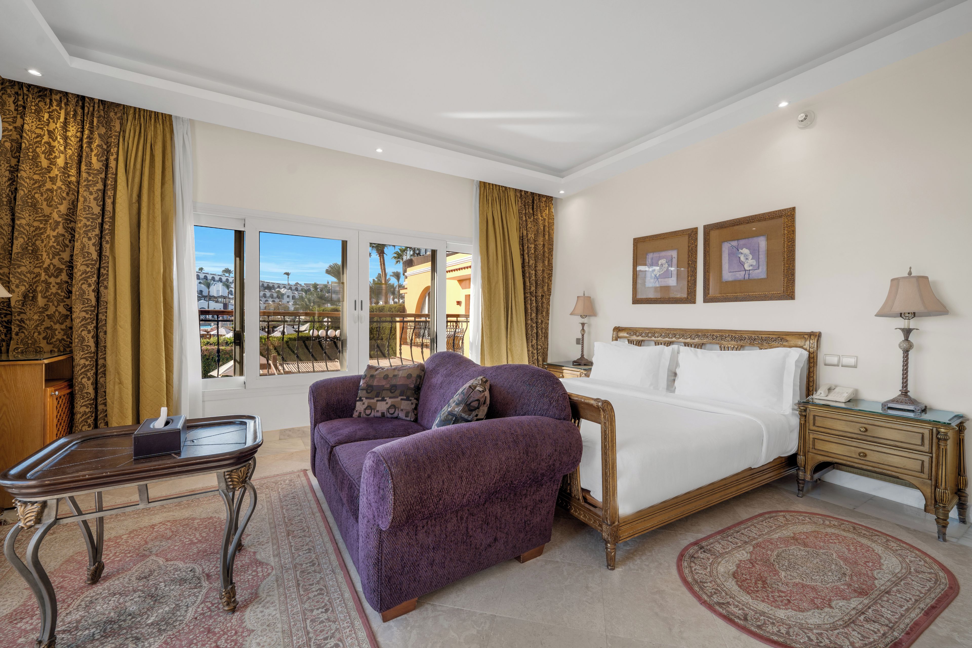 Habitación de hotel con cama, sofá, mesita de noche, lámpara y vistas al exterior.