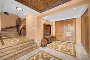 Una imponente escalera con escalones de mármol y un piso de diseño ajedrezado, que conduce a una gran puerta de madera con intrincados grabados.
