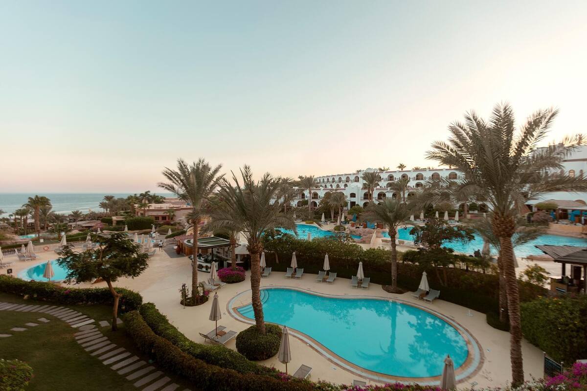 A resort with multiple swimming pools, palm trees, and a large building in the background.