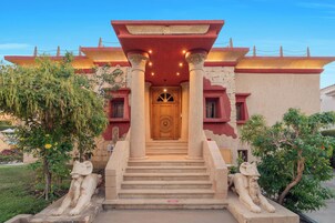 Un edificio con una entrada imponente, que presenta una gran puerta de madera, escalones que conducen a ella y dos estatuas de leones de piedra a ambos lados.