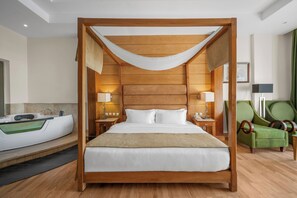 A four-poster bed with a wooden frame and white bedding, a green armchair, a side table with a lamp, and a bathtub in a hotel room. - Royal Savoy Sharm El Sheikh (Sharm El Sheikh)