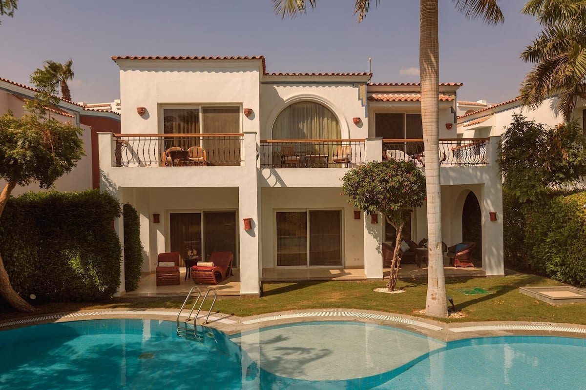 A two-story building with a swimming pool, outdoor seating, and palm trees.