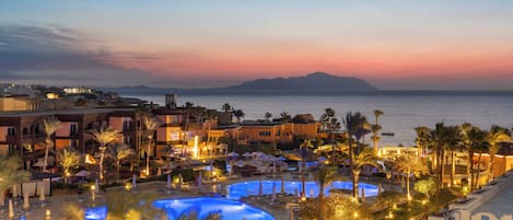 Un resort con múltiples piscinas, palmeras y vistas al mar al atardecer.