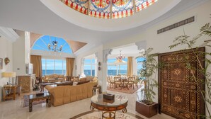 A spacious living area with a large window overlooking the sea, a chandelier, and a decorative wooden door.