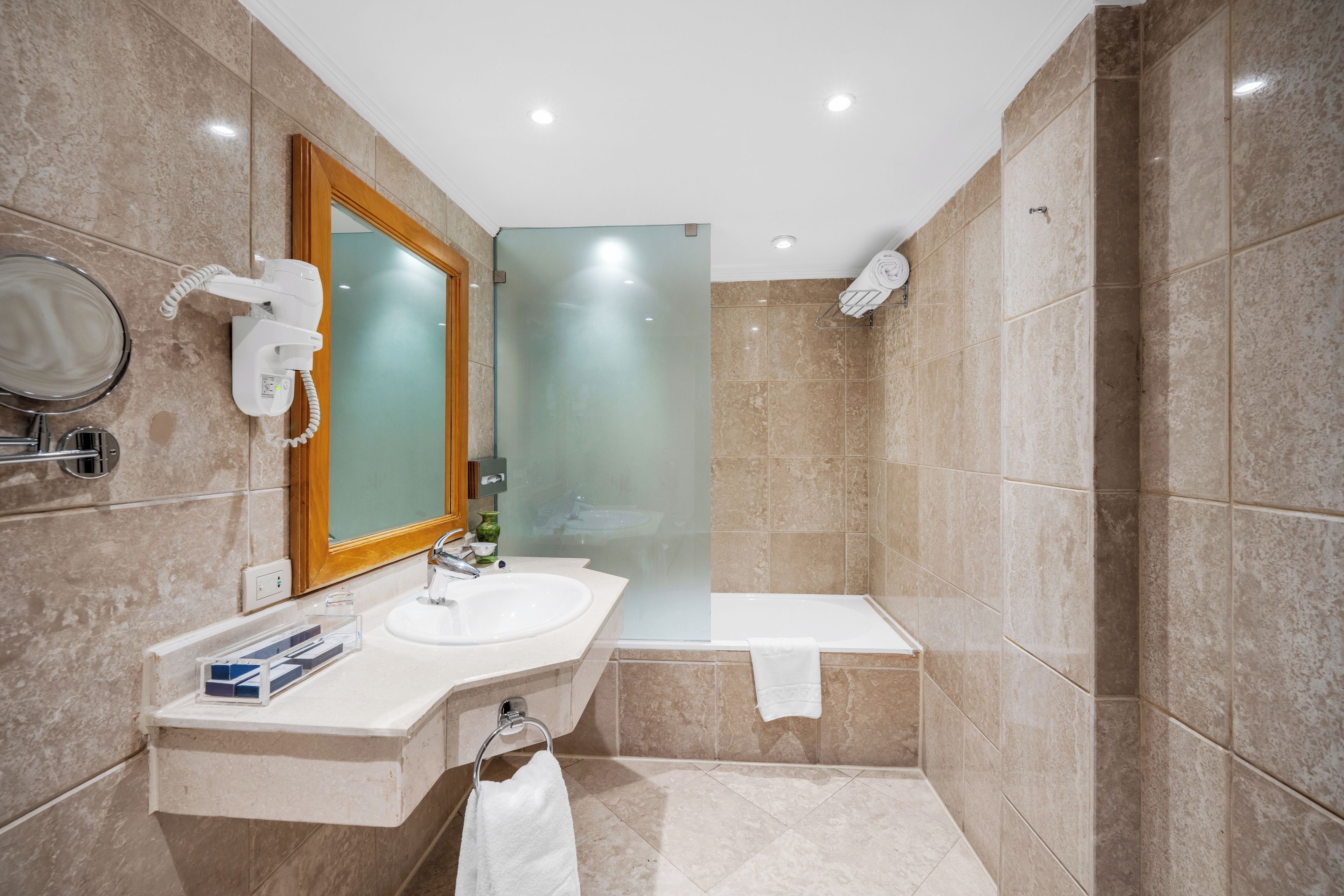 Un baño moderno con lavamanos, espejo y ducha con mampara de vidrio.