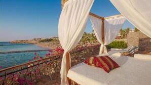 A beachside balcony with a bed, a view of the sea, and a stone wall with greenery.