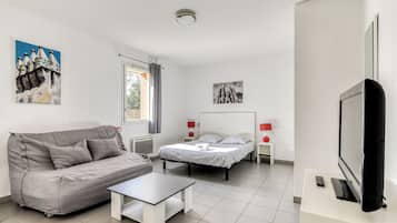 A modern bedroom with a bed, a grey sofa, a small table, and a TV.