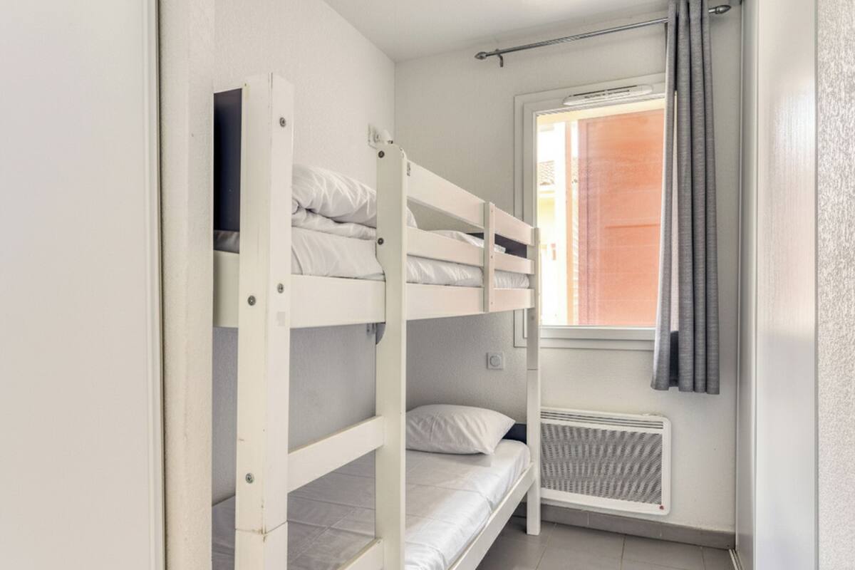 Une chambre avec un lit superposé, une fenêtre et un radiateur.