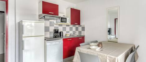 A compact kitchen with a refrigerator, microwave, and coffee maker. There is a dining table with chairs and a small television in the background.