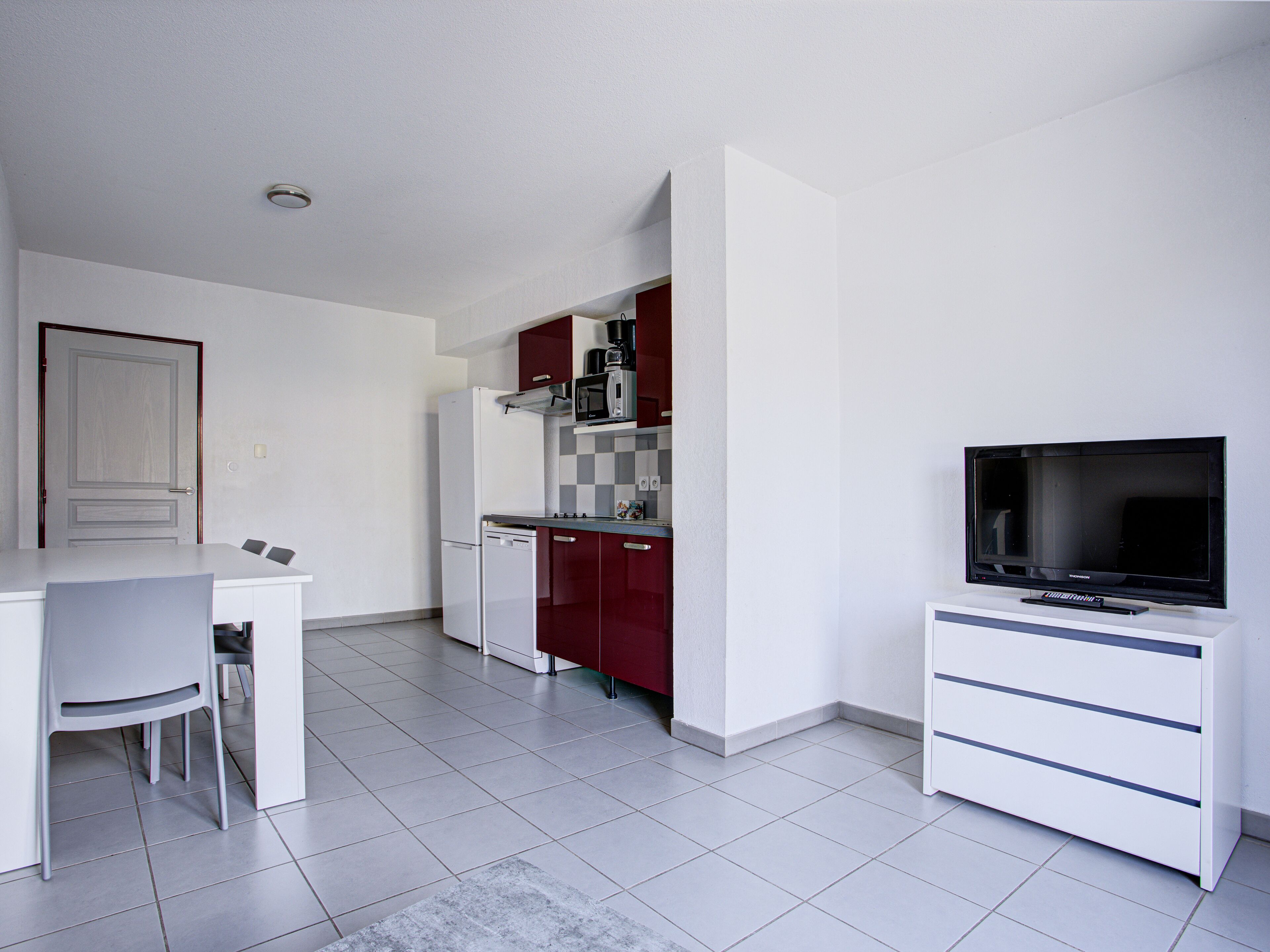 A modern kitchen with white cabinets, a red microwave, and a flat-screen TV.