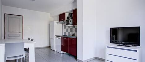 A modern kitchen with white cabinets, a red microwave, and a flat-screen TV.