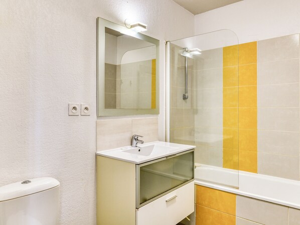 A bathroom with a white sink, a mirror, a glass-enclosed shower, and yellow-tiled walls.