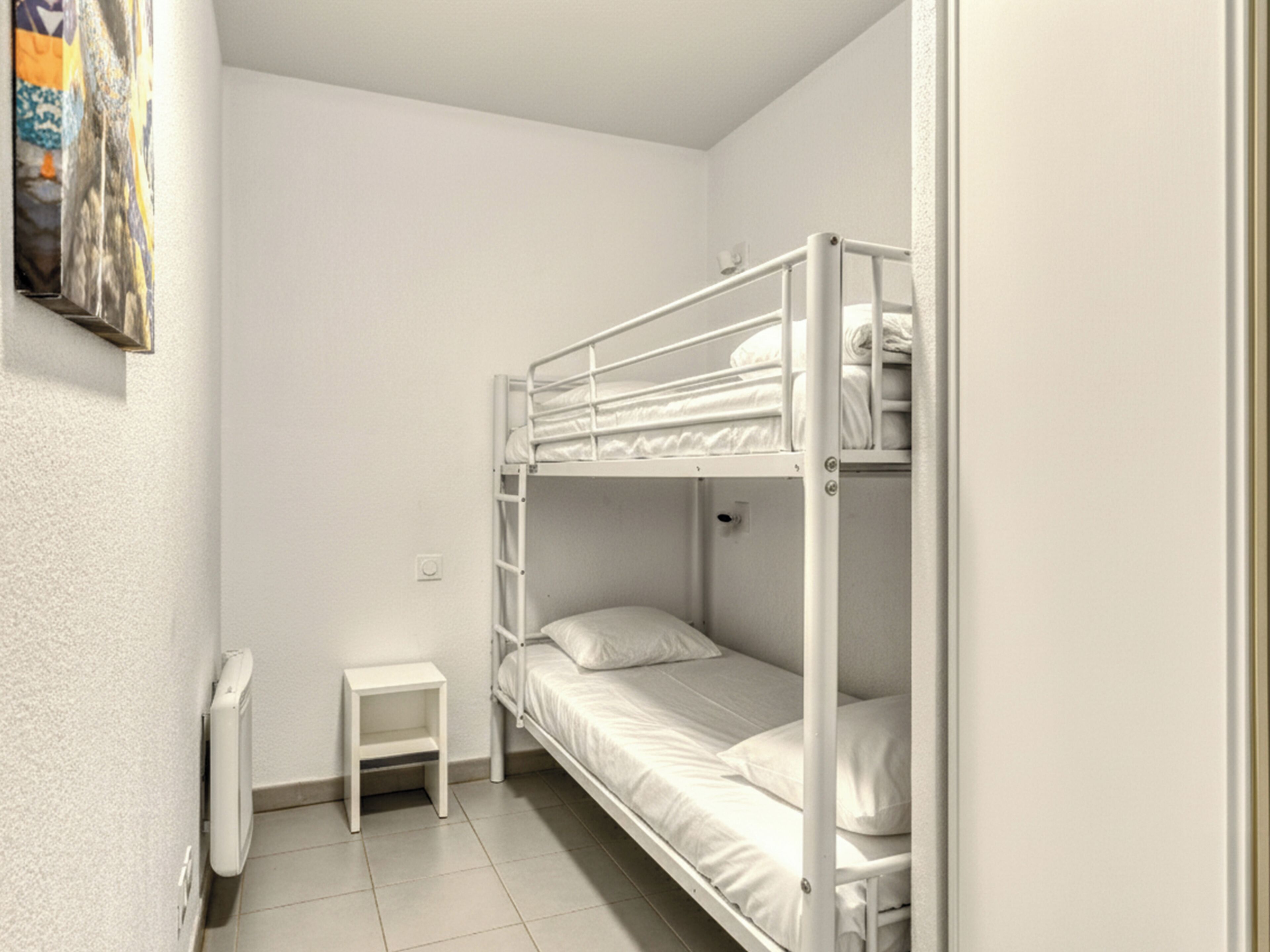 A bunk bed room with a small white nightstand and a radiator.