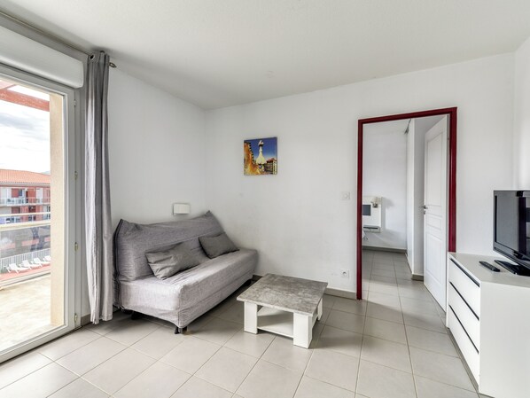 A modern living room with a grey sofa, a small white table, and a TV on a white cabinet.