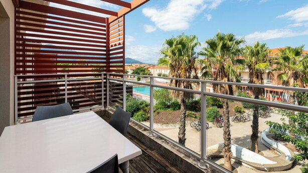 Un balcon avec une table et des chaises, donnant sur une piscine et des palmiers.