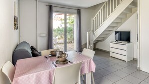 Un coin repas avec une table dressée pour quatre personnes, un escalier et un téléviseur placé dans un coin.