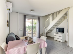 Un coin repas avec une table dressée pour quatre personnes, un escalier et un téléviseur placé dans un coin.