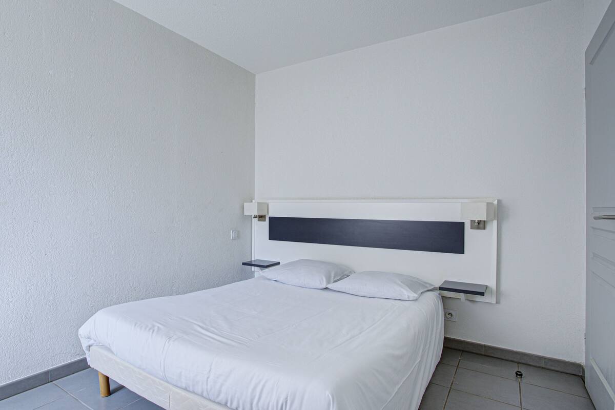 Une chambre à coucher minimaliste avec un lit simple, des murs blancs et une tête de lit sobre.