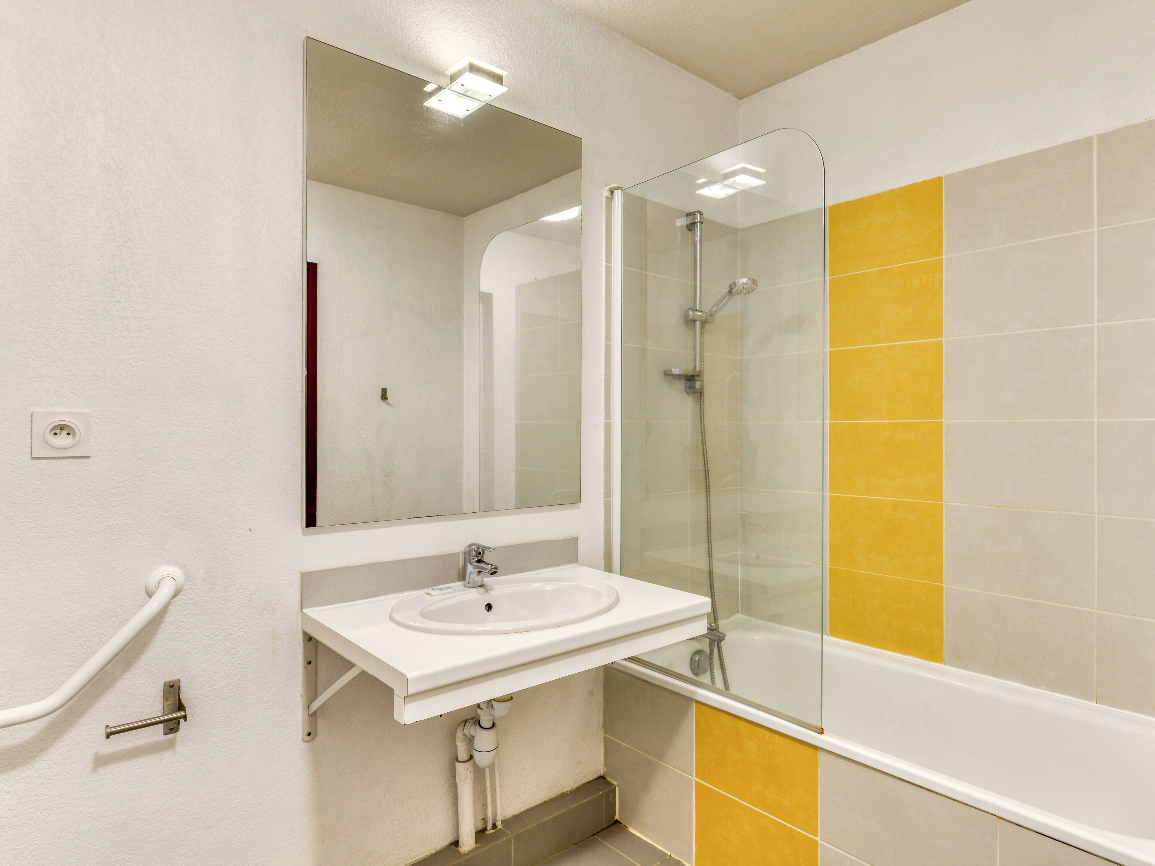Une salle de bain avec un lavabo blanc, une douche en verre et des murs recouverts de carreaux jaunes.