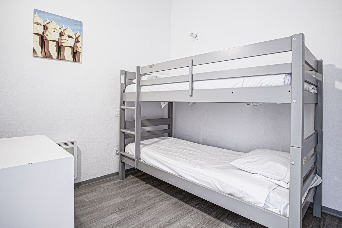 Une chambre avec un lit superposé, un bureau blanc et un tableau accroché au mur.