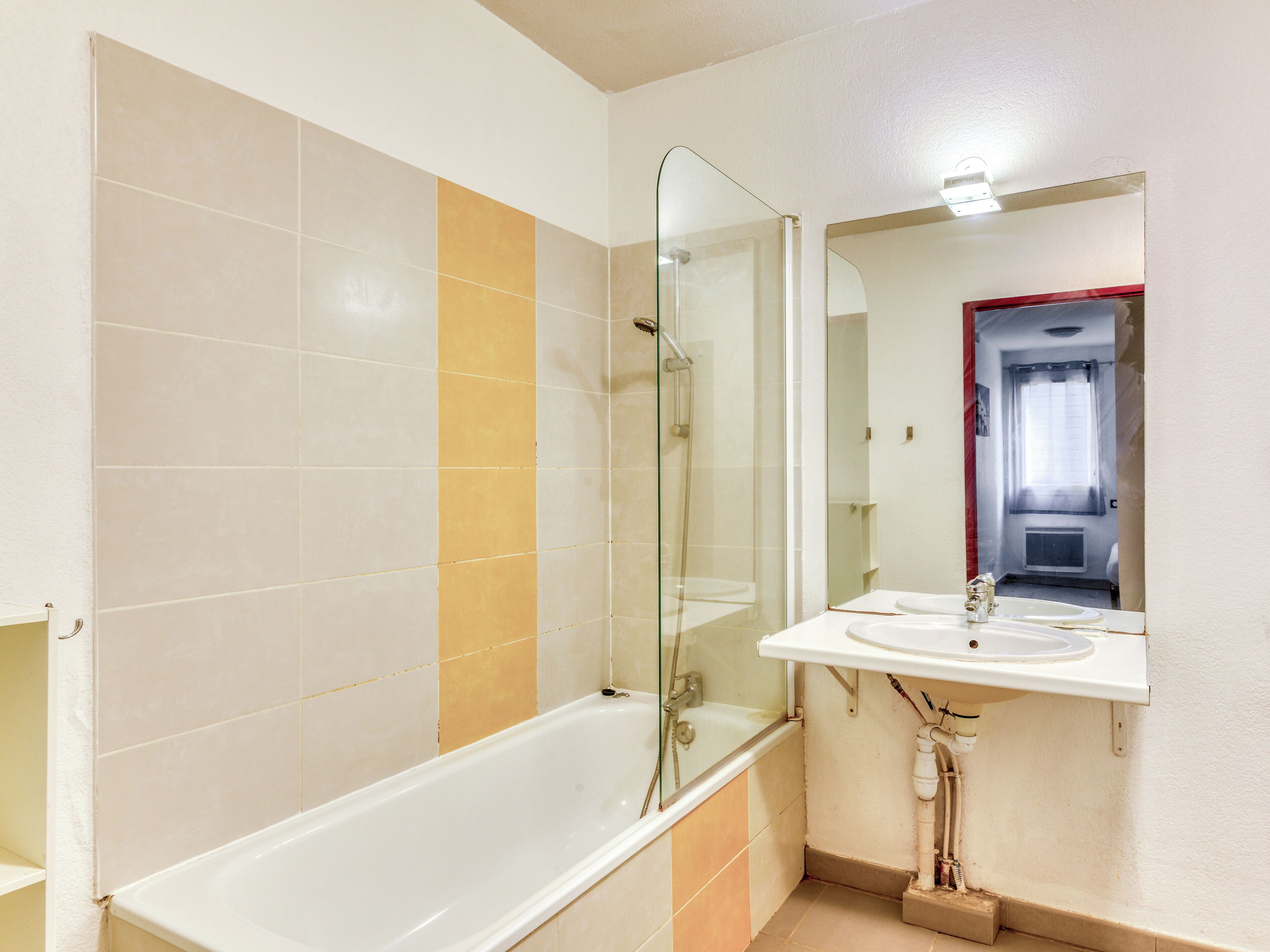 Un baño con bañera, ducha con mampara de vidrio y lavamanos con espejo arriba.