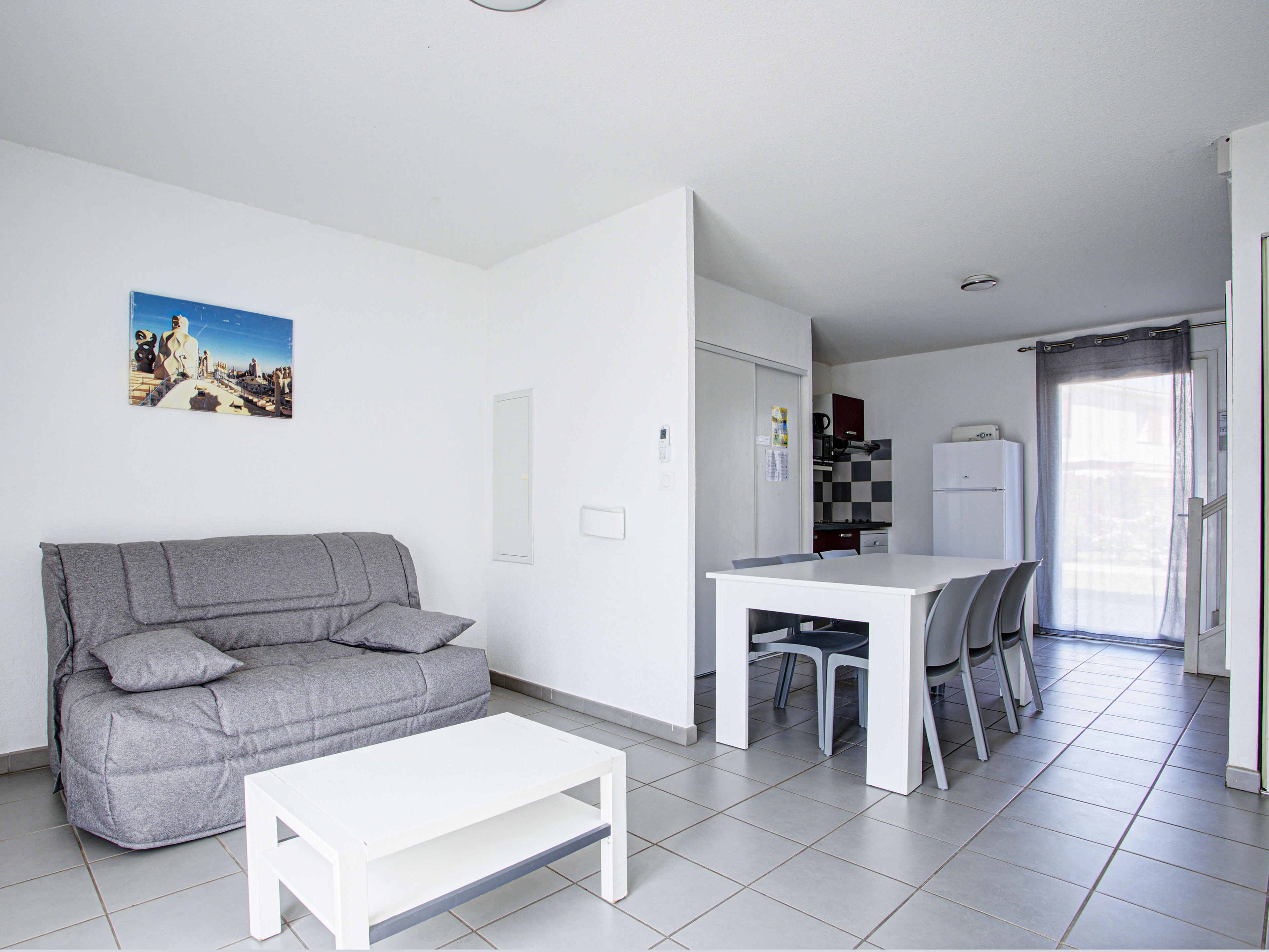 Una sala de estar moderna con un sofá gris, una mesa de centro blanca y un comedor con una mesa y sillas blancas.
