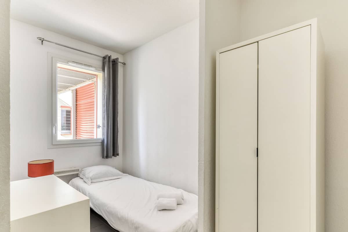 Une petite chambre avec un lit simple, une fenêtre, une table de chevet et une armoire.