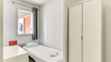Une petite chambre avec un lit simple, une fenêtre, une table de chevet et une armoire.