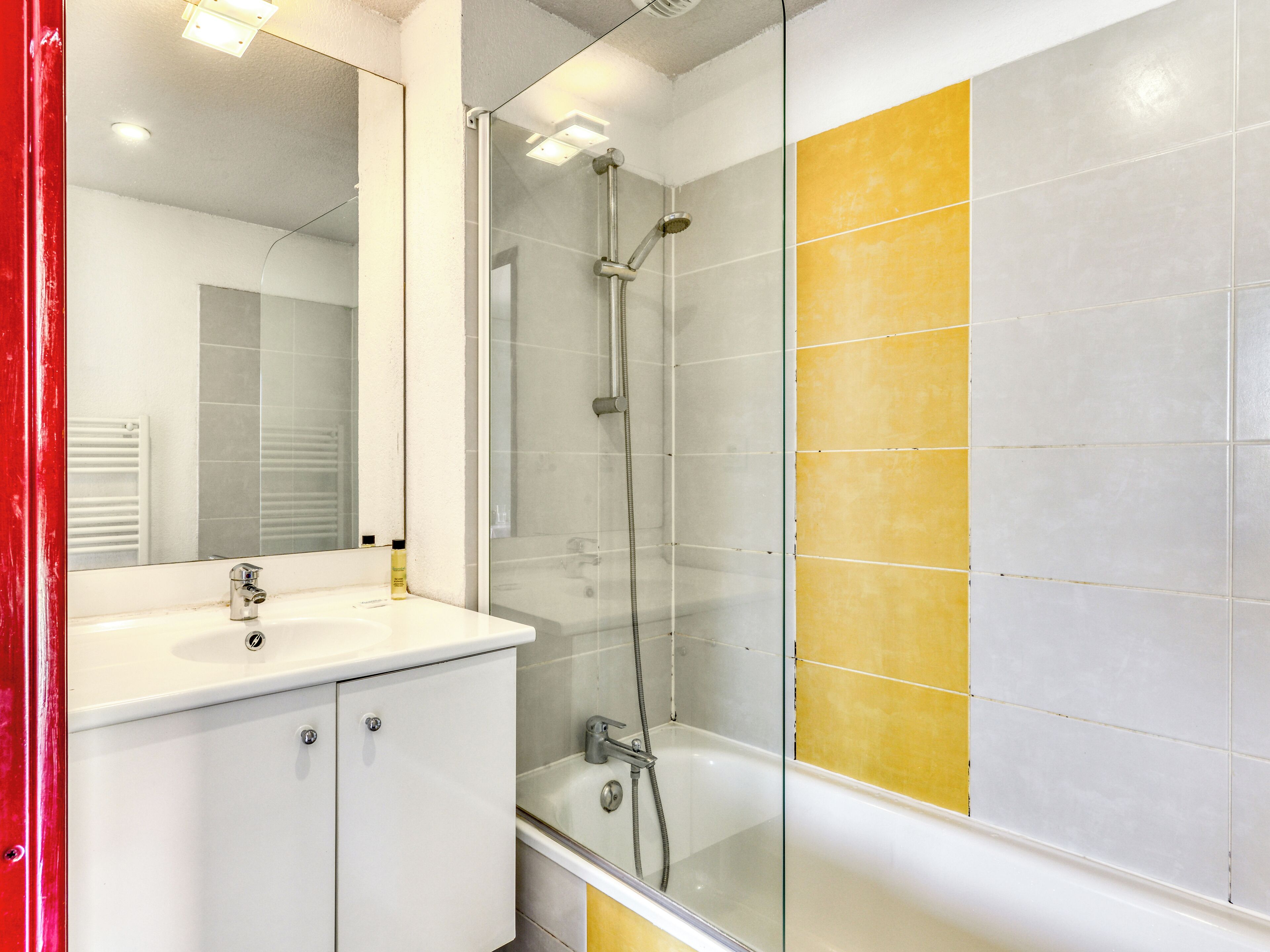 A modern bathroom with a glass-enclosed shower, a white sink, and yellow-tiled walls.