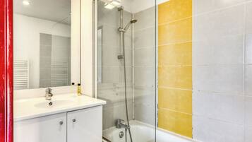 A modern bathroom with a glass-enclosed shower, a white sink, and yellow-tiled walls.