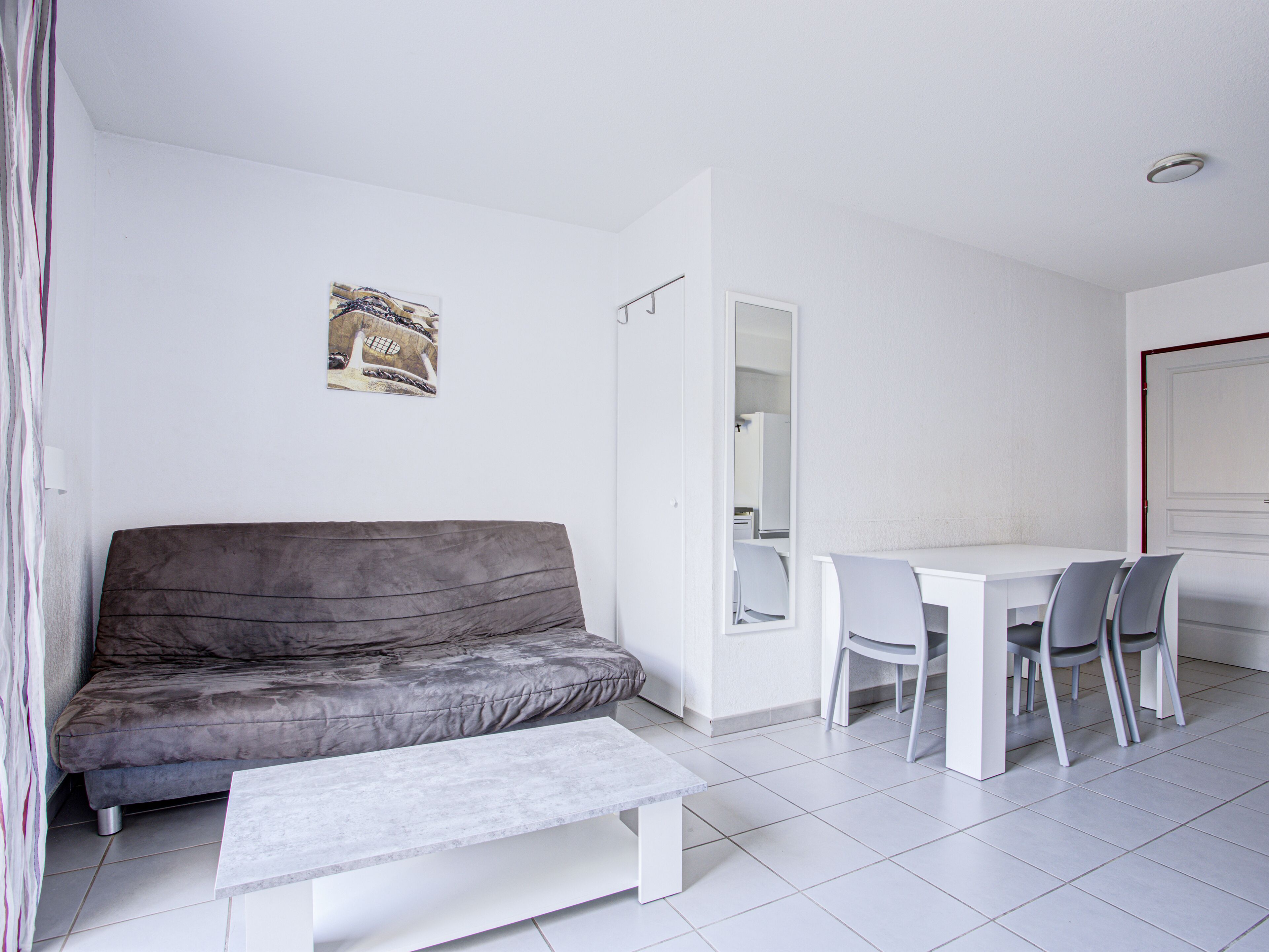 Una sala de estar moderna y minimalista con un sofá gris, una mesa de centro blanca y una zona de comedor con una mesa blanca y sillas grises.