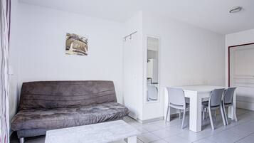 A modern, minimalist living room with a grey sofa, a white coffee table, and a dining area with a white table and grey chairs.