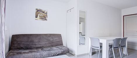 Una sala de estar moderna y minimalista con un sofá gris, una mesa de centro blanca y una zona de comedor con una mesa blanca y sillas grises.