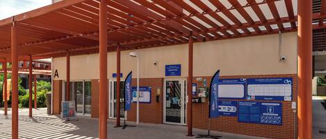 A covered outdoor area with a reception desk, informational signs, and a tiled floor.